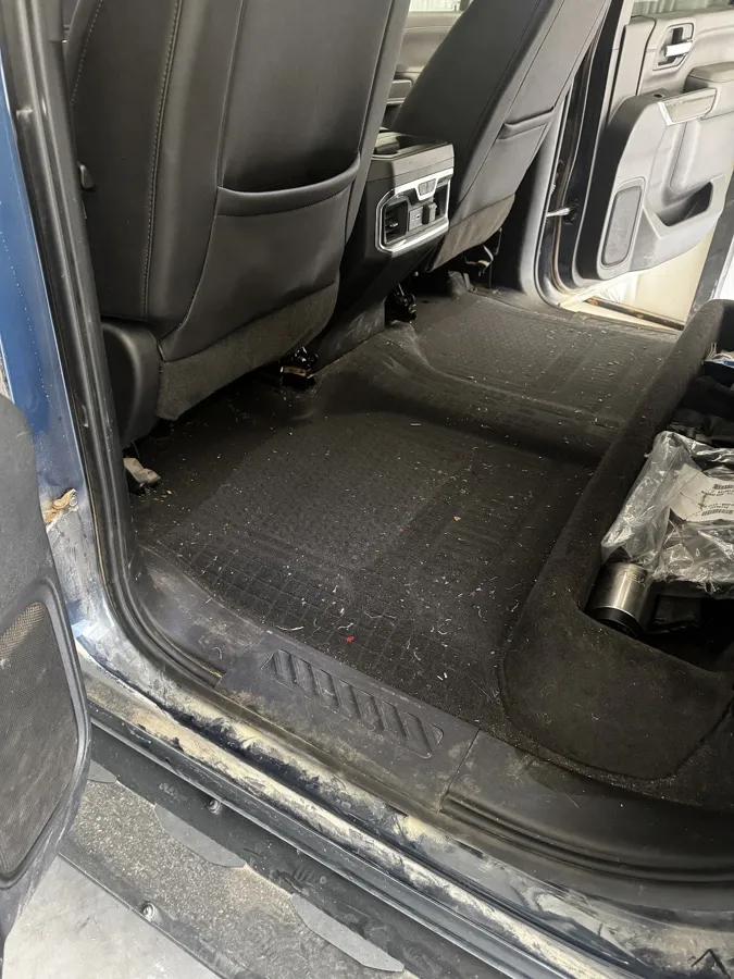 Rear floor of a GMC truck packed with dirt and debris before carpet extraction